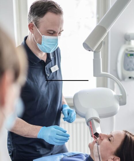 En tandläkare Örnsköldsvik iförd mask och handskar undersöker en patients tänder med hjälp av tandutrustning på en klinik.